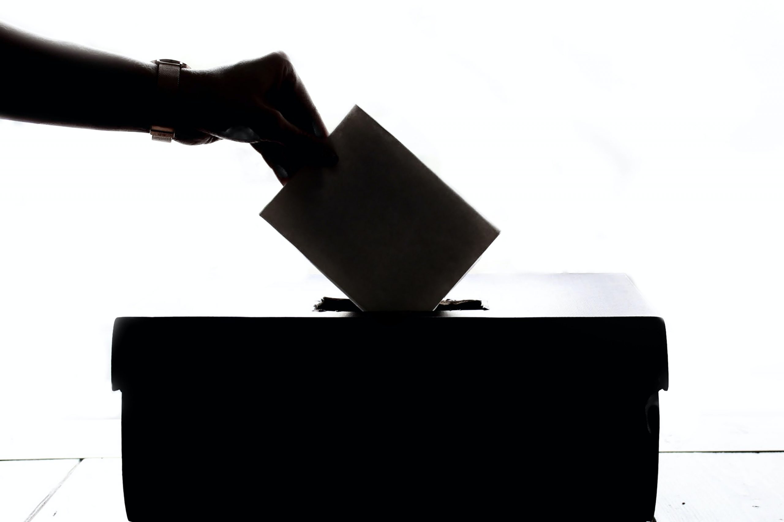 silhouette of a hand dropping a ballot card into a box