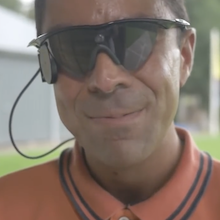 photo of a man wearing what appear to be wraparound sunglasses with a wire coming out of them
