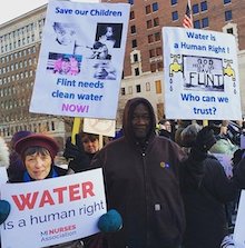 photo of people in a crowd holding protest signs reading: "Water is a human right" and "Save our children: Flint needs clean water now" and "Water is a human right: who can we trust?"